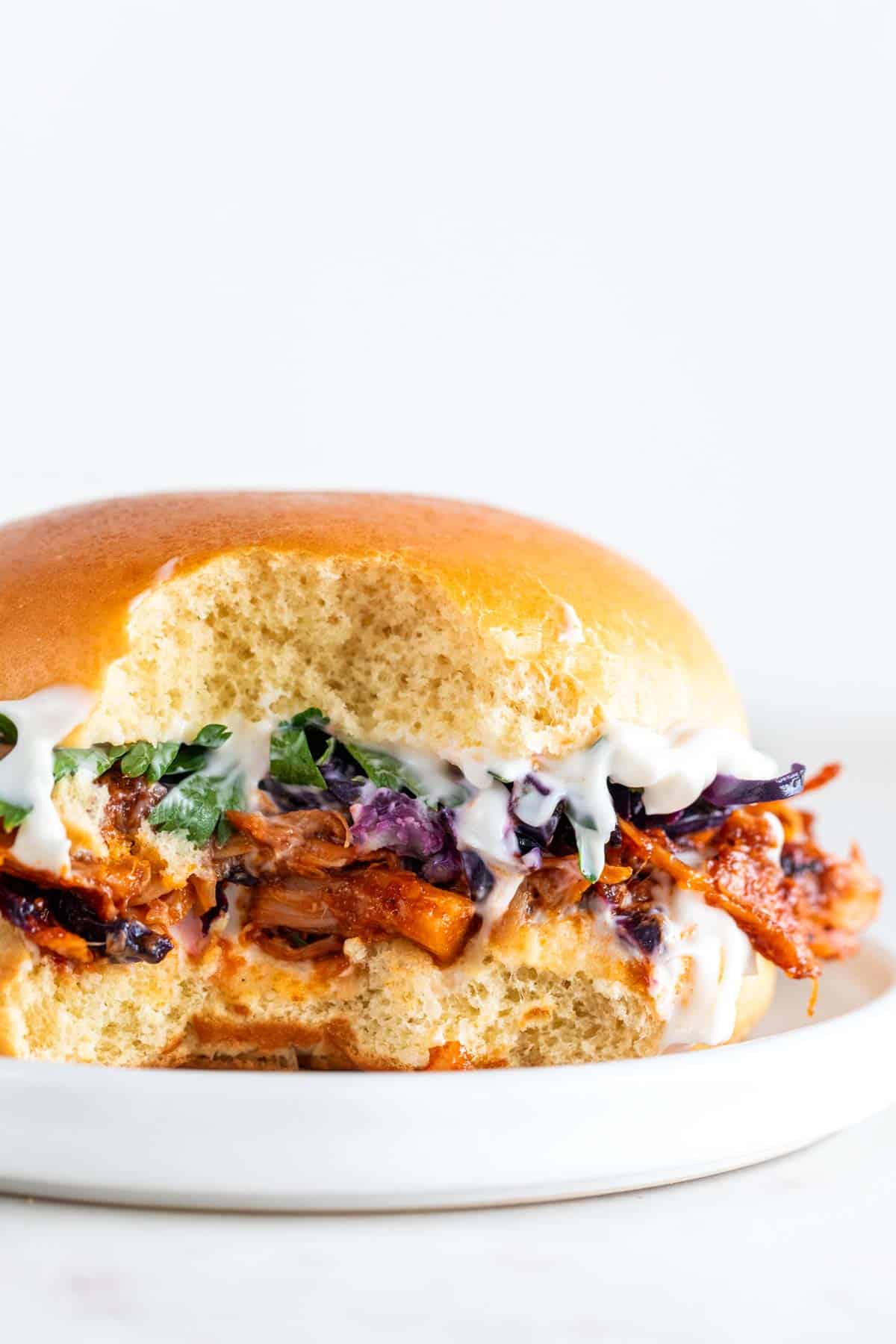 BBQ jackfruit pulled pork sandwich with vegan mayo, parsley, and red cabbage, with a bite taken.