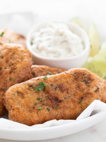 Close-up photo of a dish with beer-battered vegan fish sticks garnished with chopped parsley.