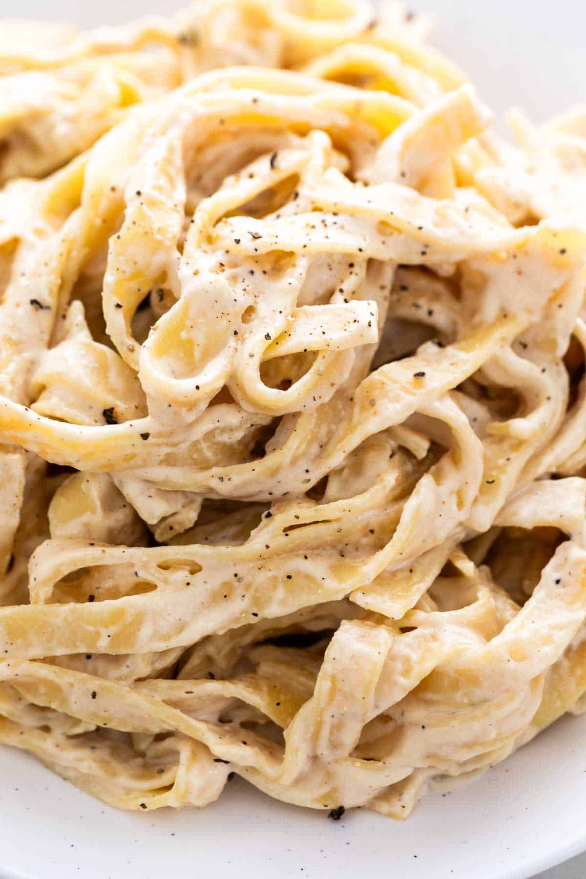 Vegan Alfredo pasta in a dish garnished with ground black pepper.