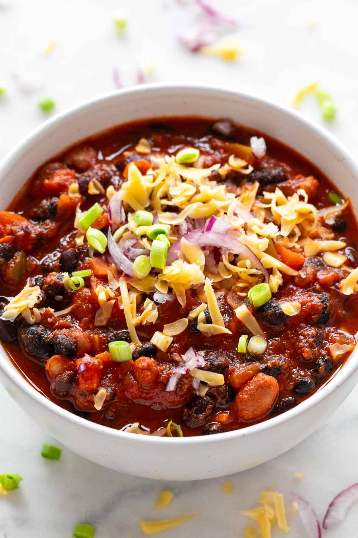 Bowl with vegan chili topped with fresh green onions and vegan shredded cheese.