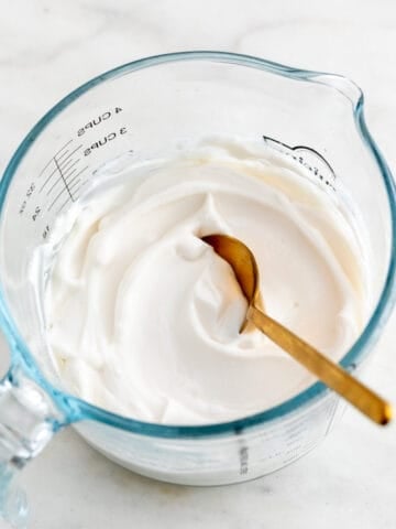A glass measuring cup with vegan mayonnaise and a spoon.