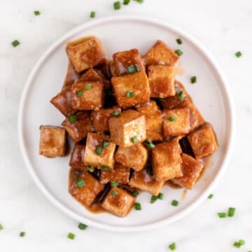 Square picture of a dish with marinated tofu garnished with chopped chives.