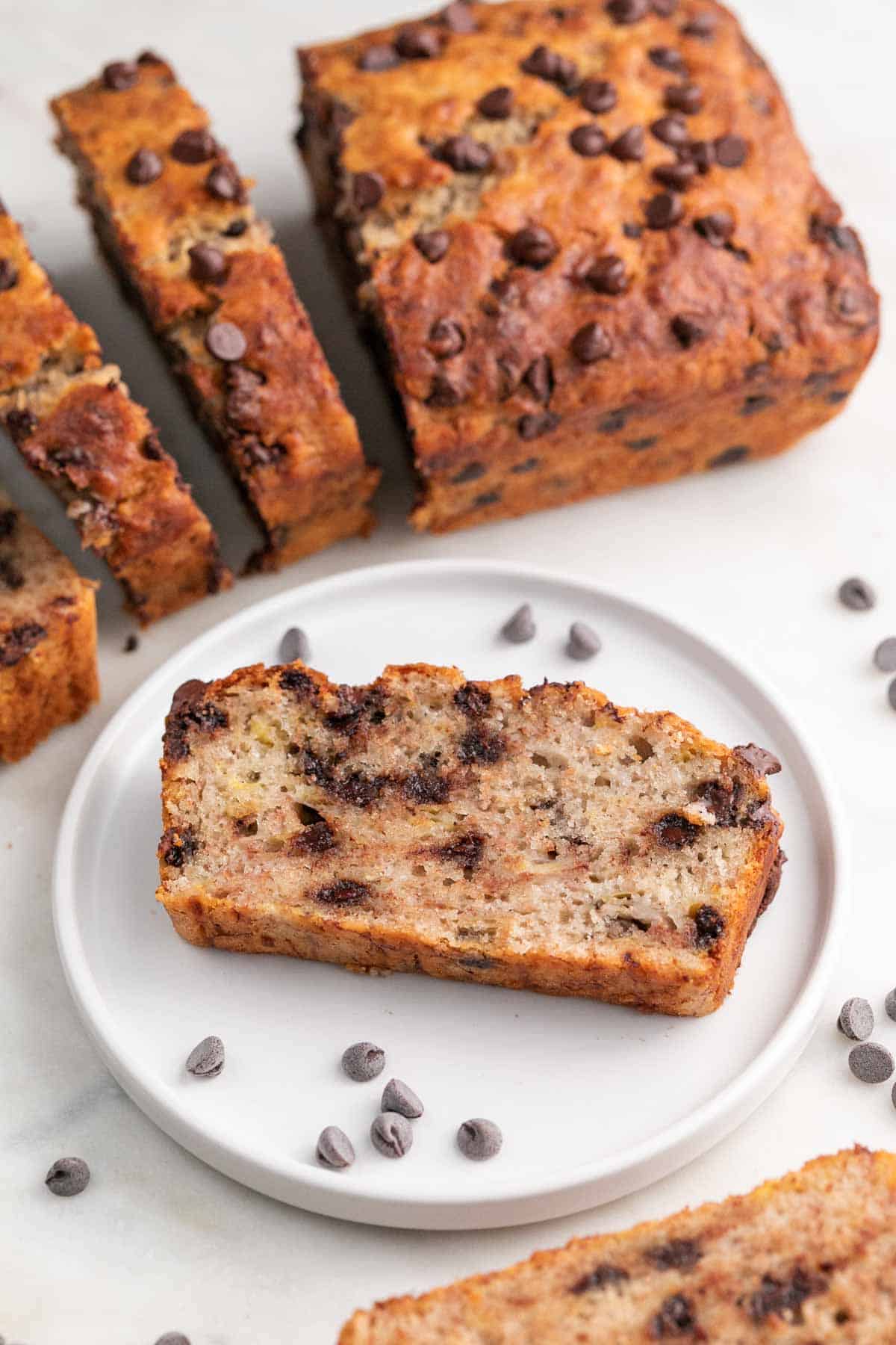 Plate with a slice of vegan banana bread and sliced loaf in the background.