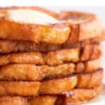 Stalk of vegan French toast on a plate with some maple syrup and vegan butter on top.