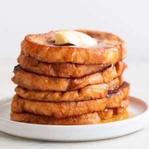 Stalk of vegan French toast on a plate with some maple syrup and vegan butter on top.