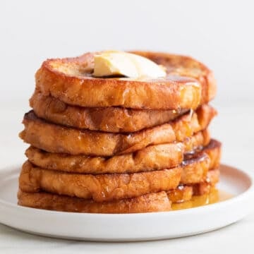 Stalk of vegan French toast on a plate with some maple syrup and vegan butter on top.