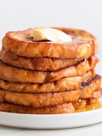 Stalk of vegan French toast on a plate with some maple syrup and vegan butter on top.