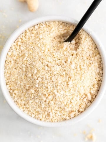 White bowl of vegan Parmesan cheese with a serving spoon.