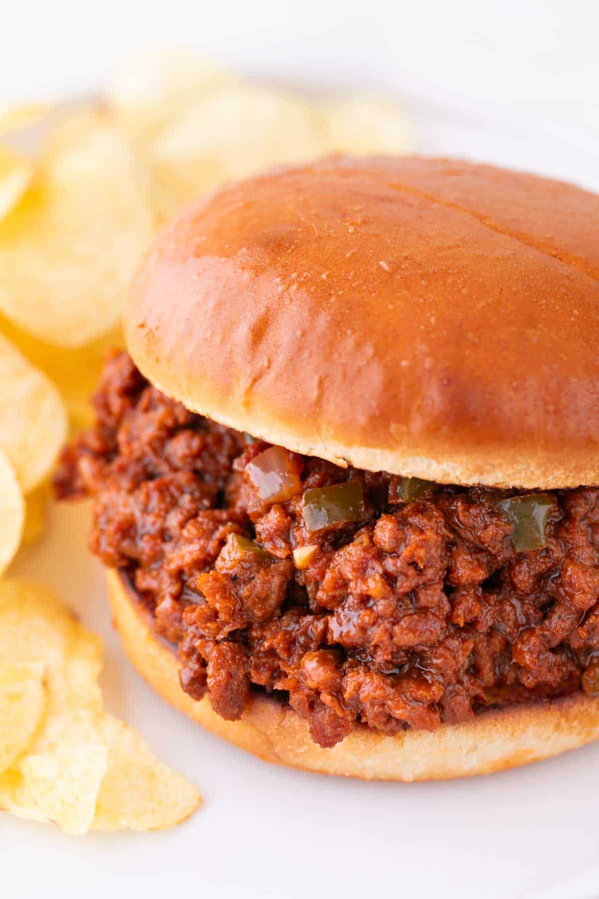 Vegan sloppy joes on white dish, accompanied by crispy potato chips.