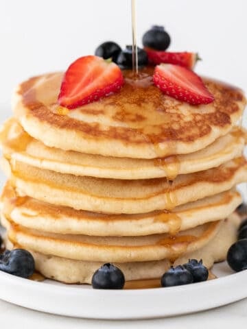 Vegan pancakes heaped with strawberries, blueberries, and maple syrup drizzle.