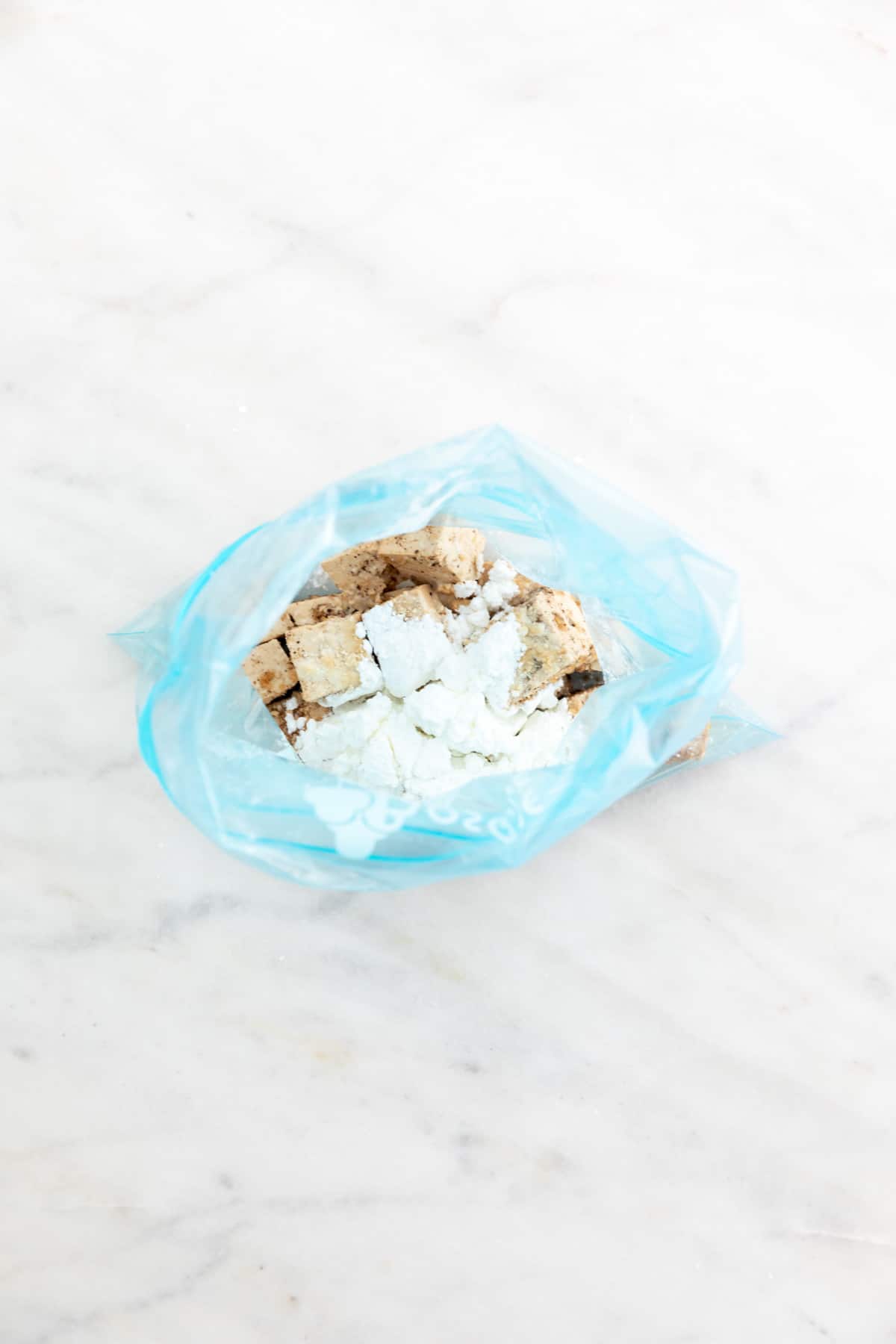 Seasoned tofu cubes in a freezer bag with some cornstarch on top.