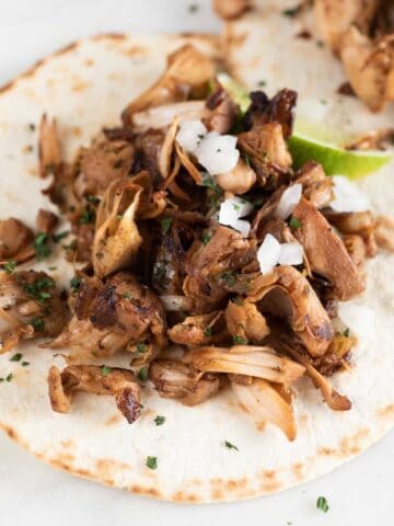 Close-up photo of a jackfruit carnita with a lime wedge, chopped cilantro and diced onion