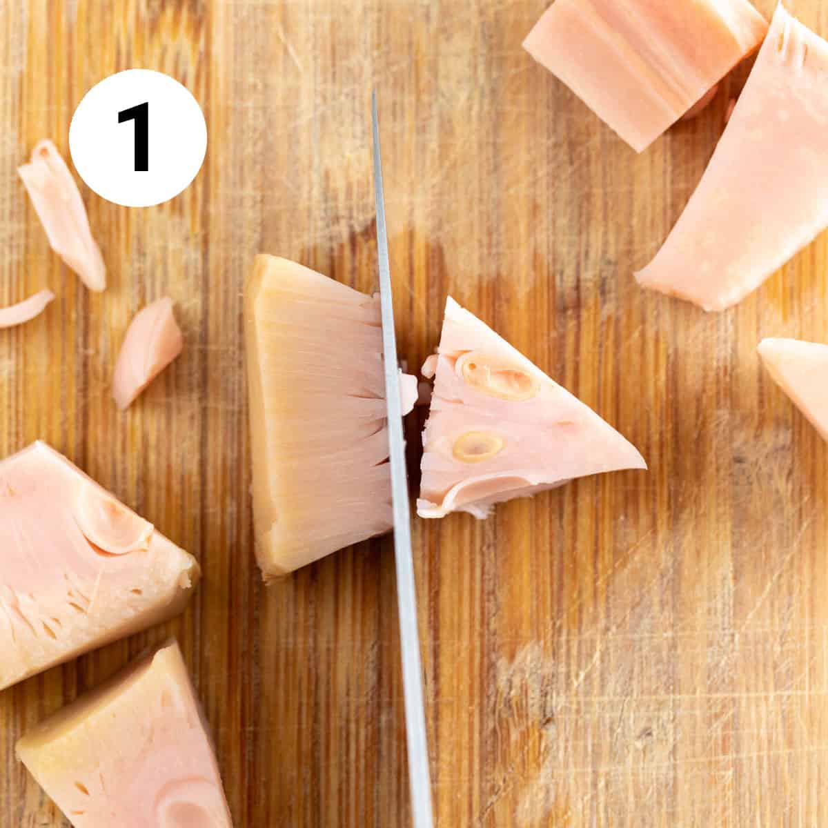 Knife chopping jackfruit on wooden cutting board.