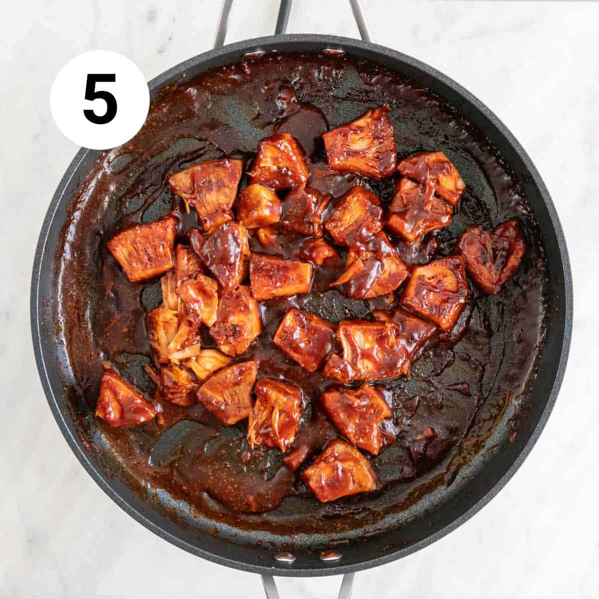 Sautéed jackfruit in a skillet with spices and BBQ sauce.