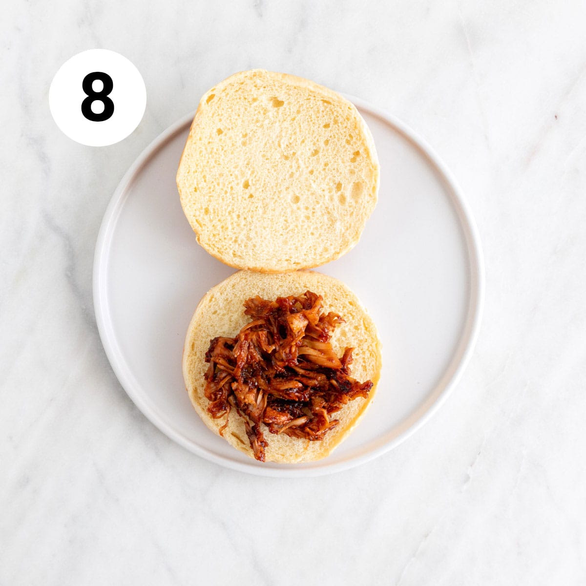 BBQ jackfruit pulled pork on a hamburger bun on a plate.