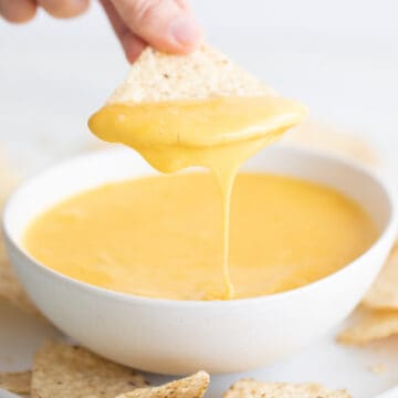 Bowl of vegan cheese with a hand dipping a tortilla chip.