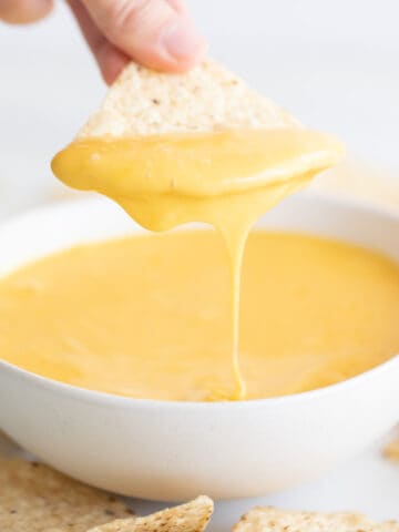 Bowl of vegan cheese with a hand dipping a tortilla chip.