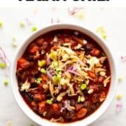 Bowl of vegan chili featuring green onions, red onion, and vegan shredded cheese.