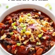 Vegan chili in a bowl garnished with green onions, red onion, and vegan cheese.