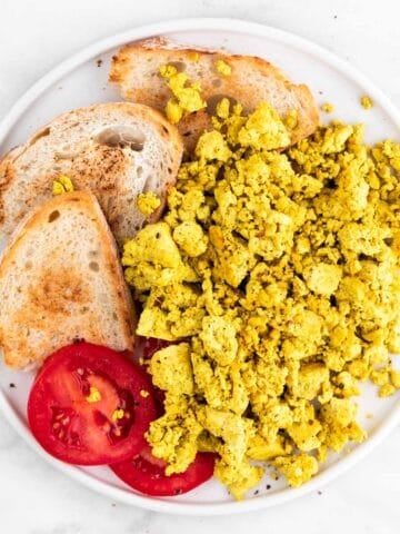 Tofu scramble, bread, and tomato slices arranged in a white dish.
