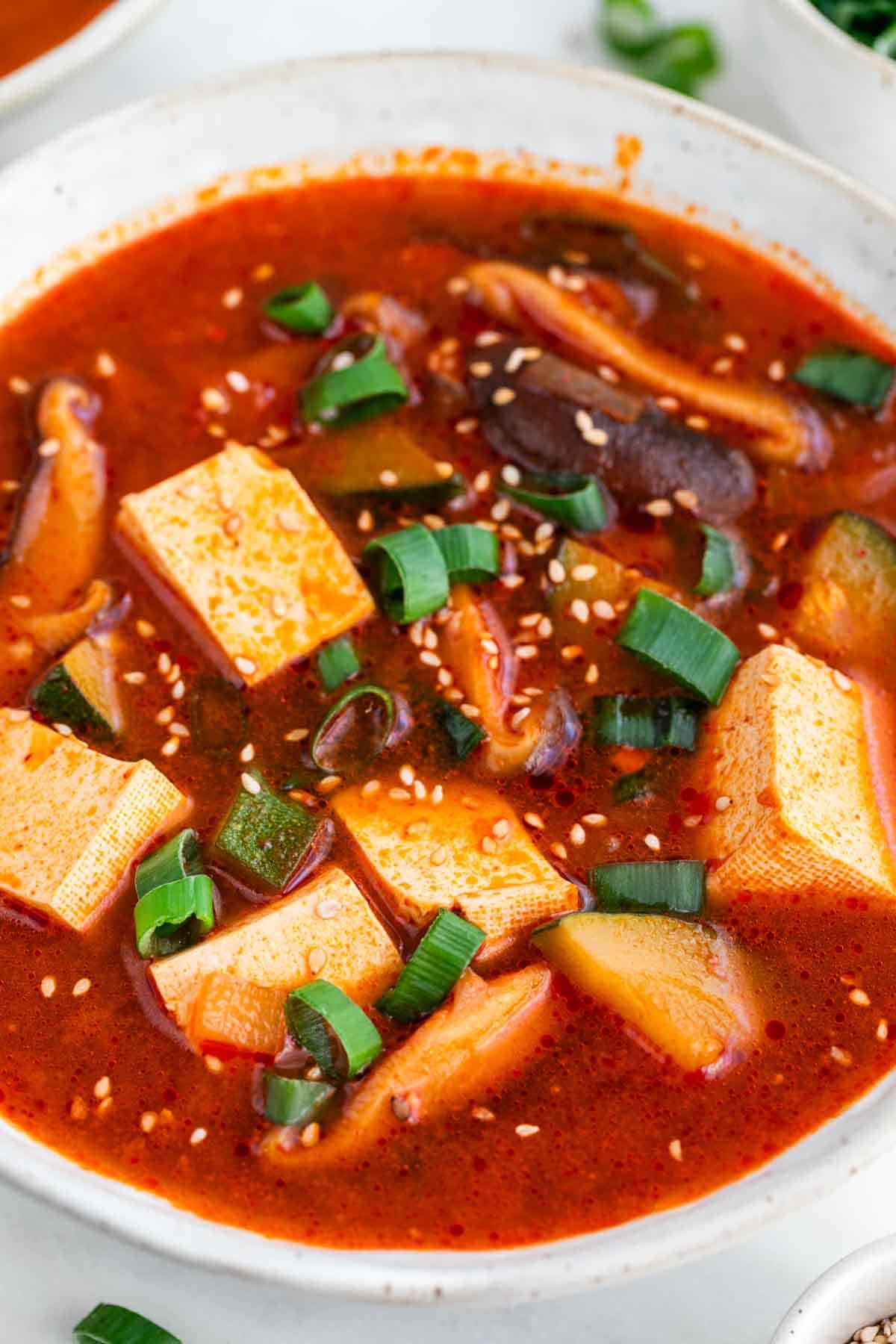 Bowl of spicy Korean tofu soup garnished with scallions and sesame seeds.