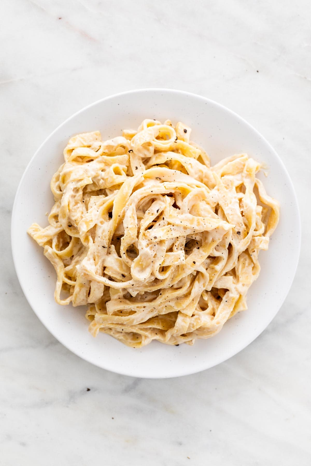 Plate of pasta with vegan cashew alfredo sauce topped with ground black pepper.