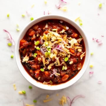 Vegan chili presentation with fresh green onions, red onion, and vegan cheese.