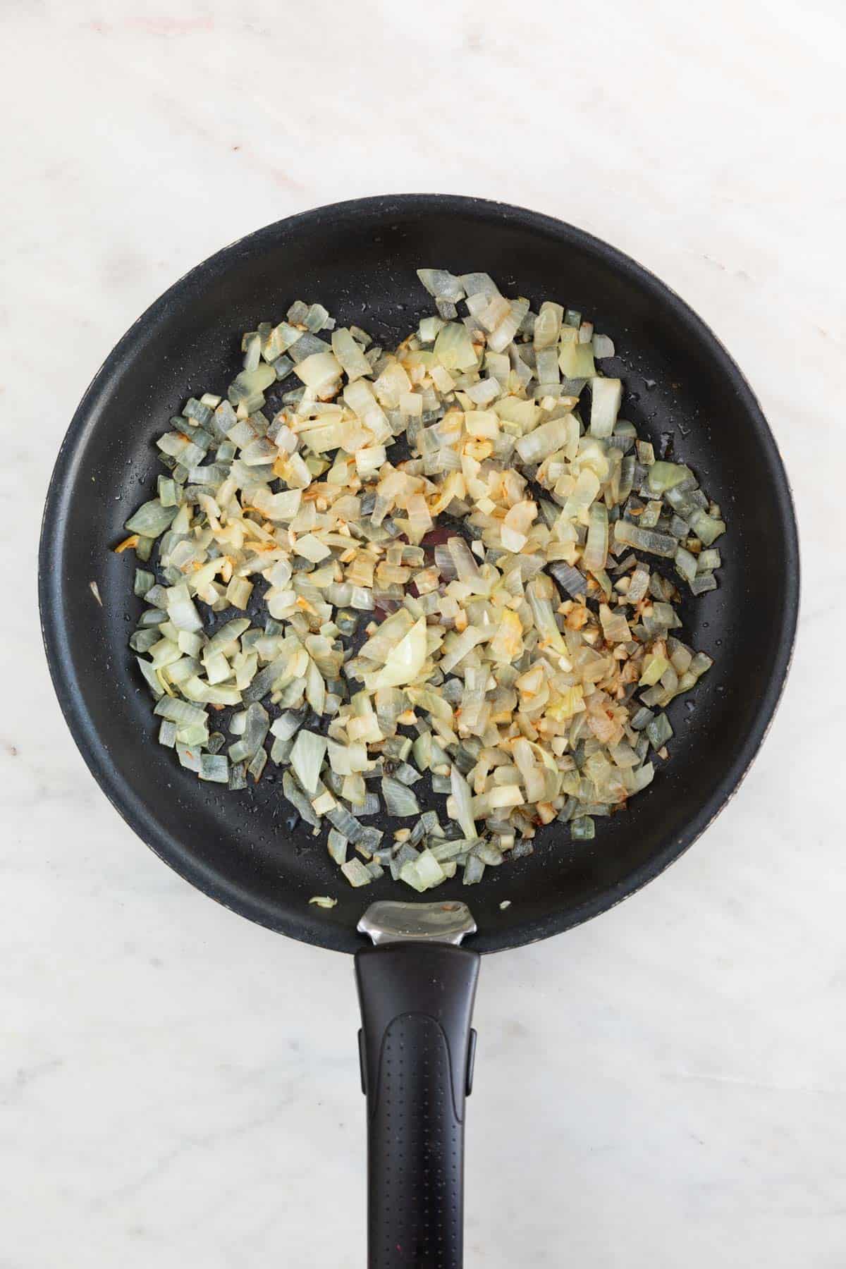 A skillet with cooked onion and garlic.