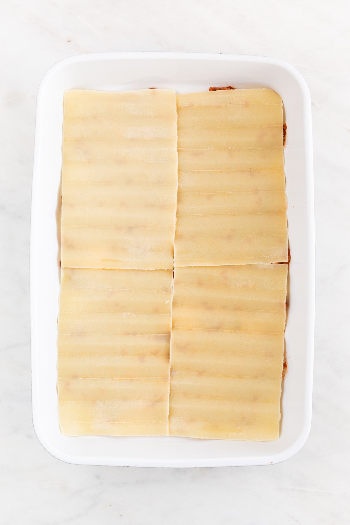 A casserole dish with 4 lasagna noodles on top of the vegan meat sauce.