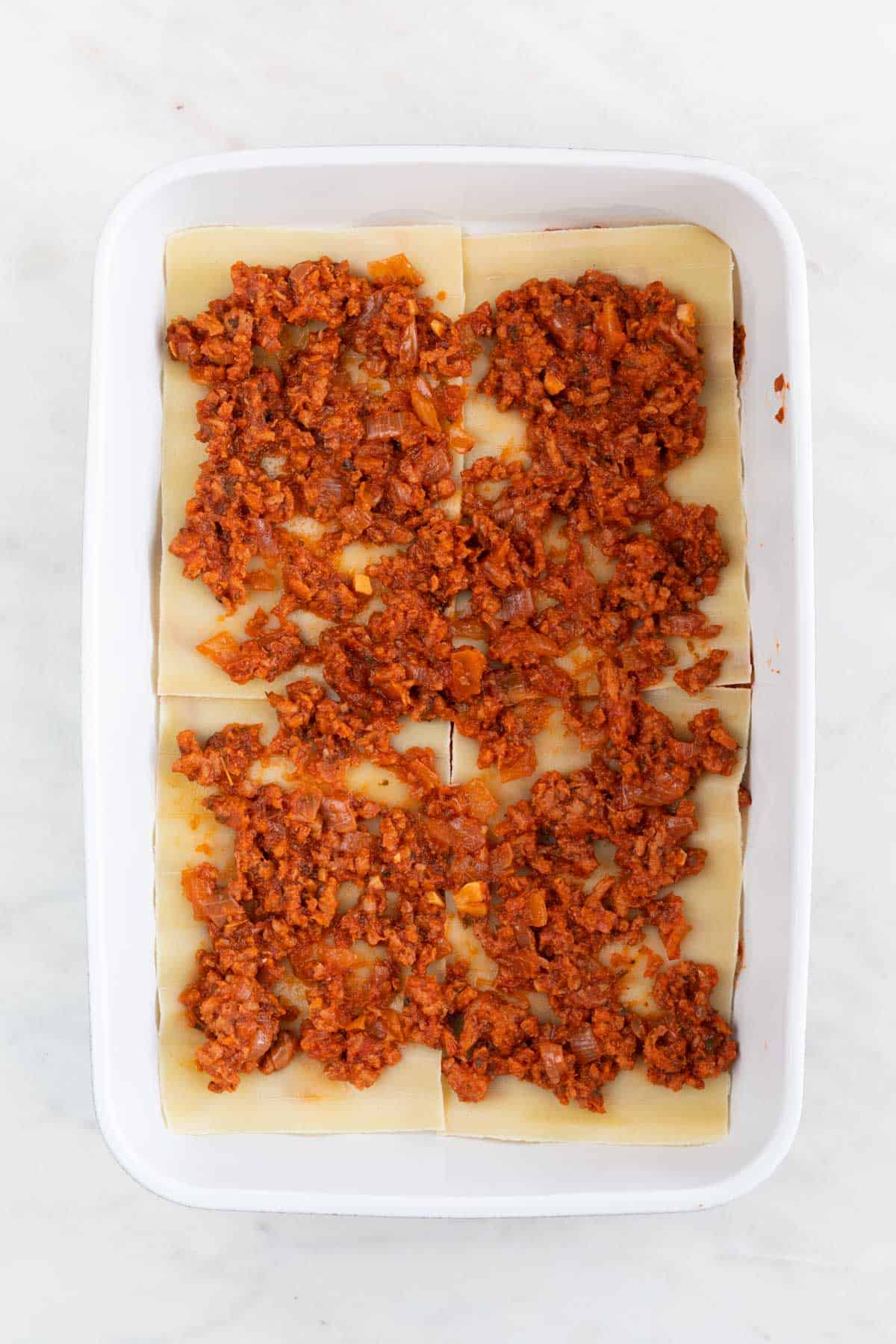 A casserole dish with a layer of vegan meat sauce.