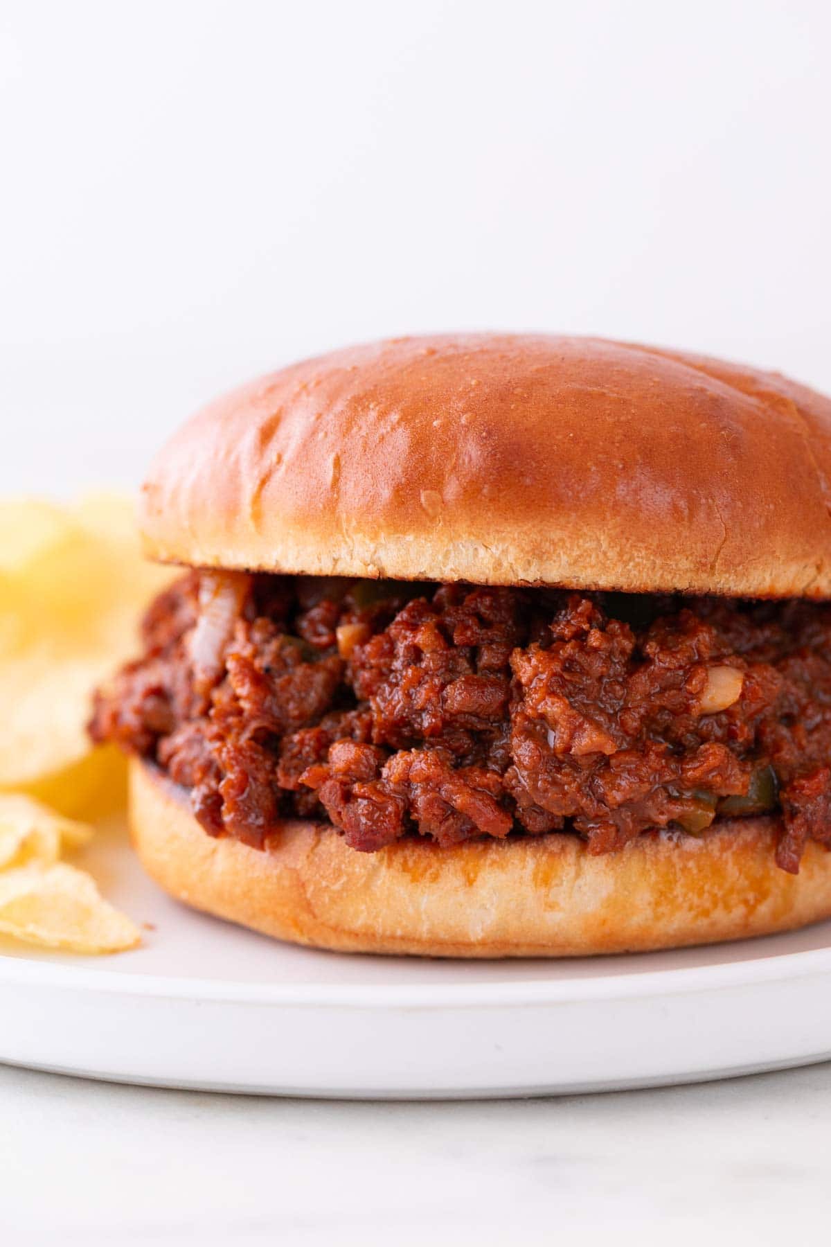 Vegan sloppy joe sandwich on a white plate with a side of potato chips.