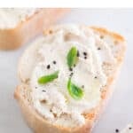 A slice of bread spread with some vegan tofu ricotta cheese and some basil leaves and black pepper on top.